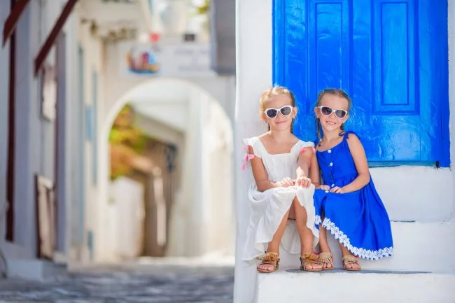 cute little girls at street of typical greek traditional village with white walls and colorful doors on Mykonos Island, in Greece